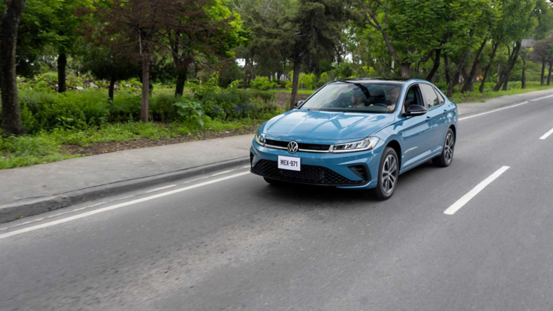 Jetta 2026 de color azul transita sobre avenida rodeada por un jardín. 