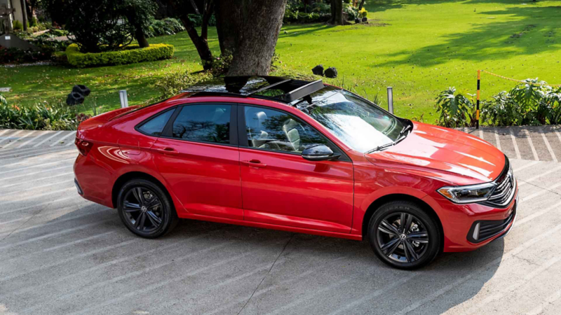 Volkswagen Jetta en color rojo y techo negro estacionado cerca de una jardinera. 