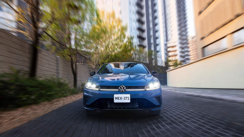 Volkswagen Jetta de color azul transita en una calle dentro de una zona de edificios. 
