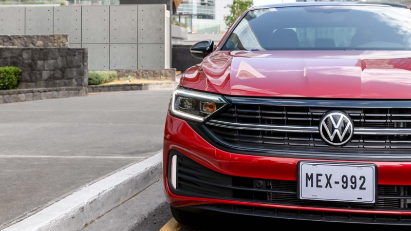 Jetta Volkswagen seminuevo de color rojo a las afueras de edificio de concreto.