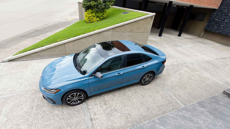 Volkswagen Jetta de color azul. Vista cenital del sedán estacionado en la entrada de una residencia moderna.