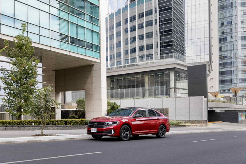 Jetta seminuevo de color rojo circula en una avenida dentro de zona urbana moderna con rascacielos.