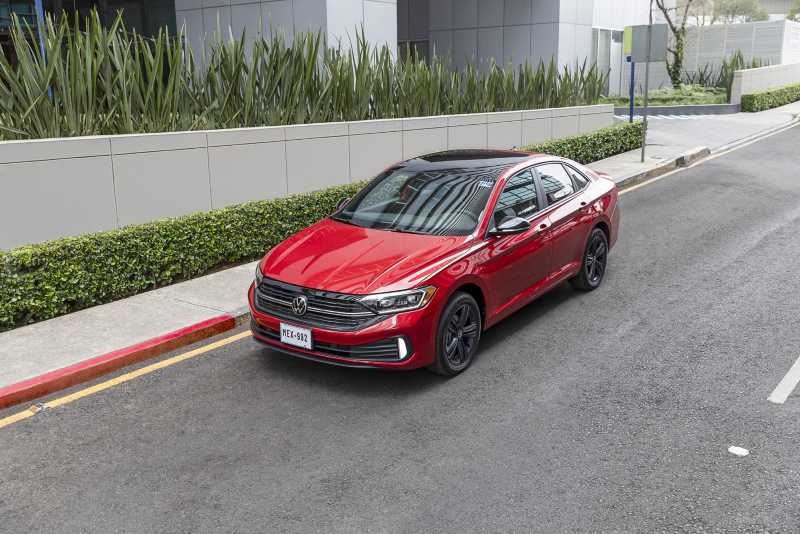 Jetta rojo estacionado cerca de jardinera de edificio moderno.