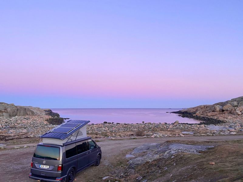 En VW California står parkerad vid kusten med rosa horisont