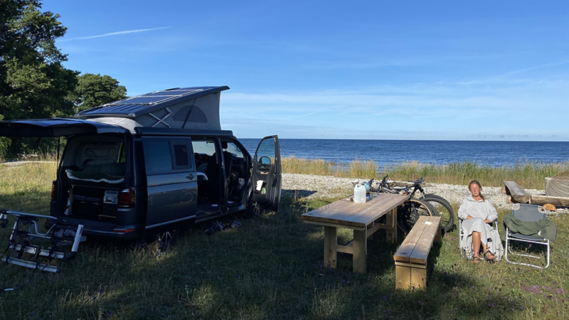 Kvinna solar vid en parkerad VW California campingbil