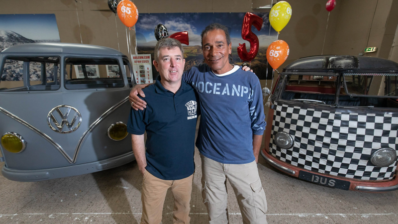 John and Riki standing in front of their VW Samba vans.
