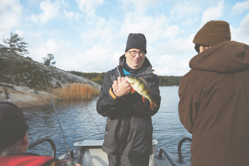 En person håller i en aborre på en båt ute på sjön i naturnära omgivning