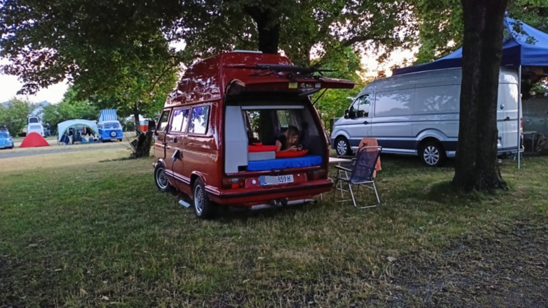 Jürgens roter VW T3 mit offener Heckklappe auf einem Campingplatz.