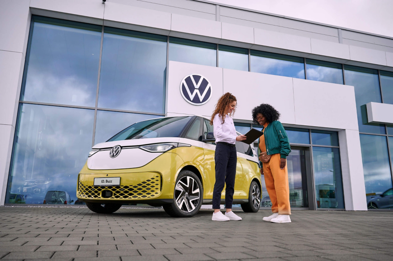 A VW service employee and customer standing next to an ID. Buzz, parked outside a Van Centre