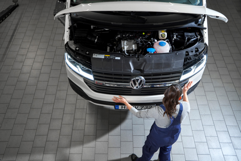 Pracownica serwisu stoi przed dostawczym Volkswagenem z otwartą maską.