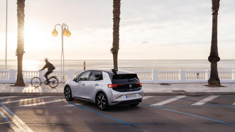 Elektroauto parkt an einer Küstenstrasse mit Palmen bei Sonnenaufgang
