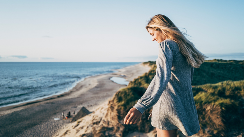 Jeune femme souriant sous le soleil sur la côte.