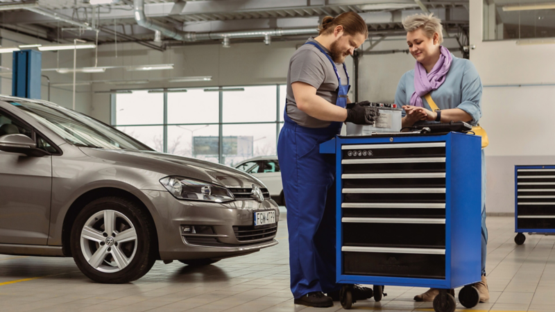 pracownik i klientka pochylający się nad skrzynią z narzędziami, w tle serwisowany samochód