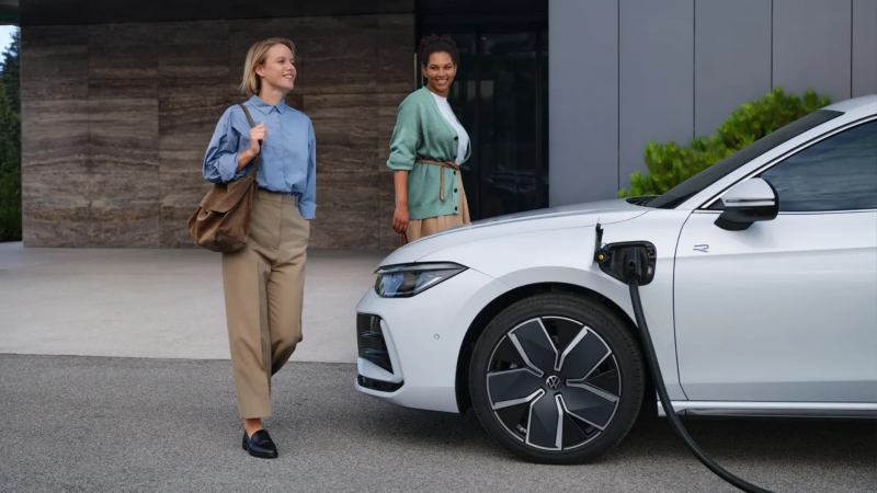 2 vrouwen lopen naast een Volkswagen die wordt opgeladen, ze hebben nette kleding aan