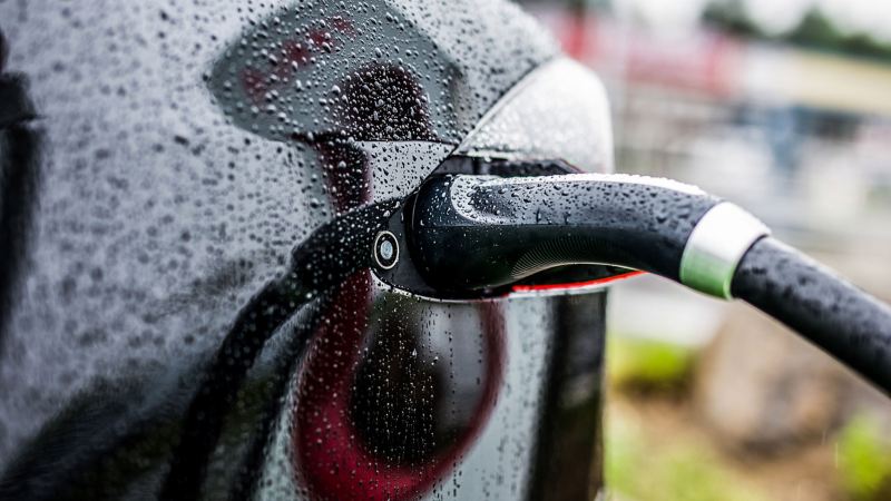 Ein Ladestecker voller Regentropfen steckt in einem Elektroauto. 