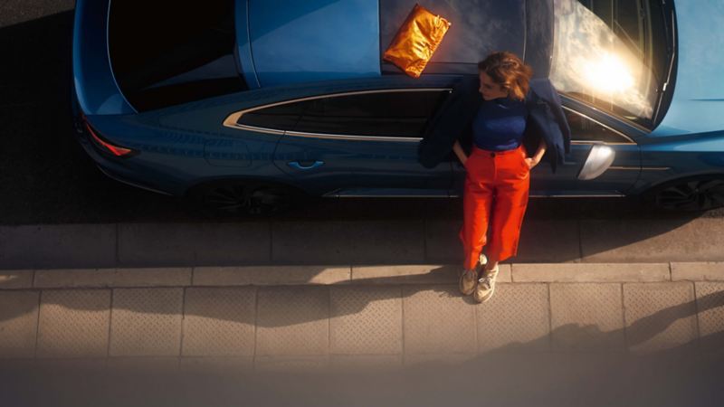 Vista superior de una chica al lado de un Volkswagen Arteon azul