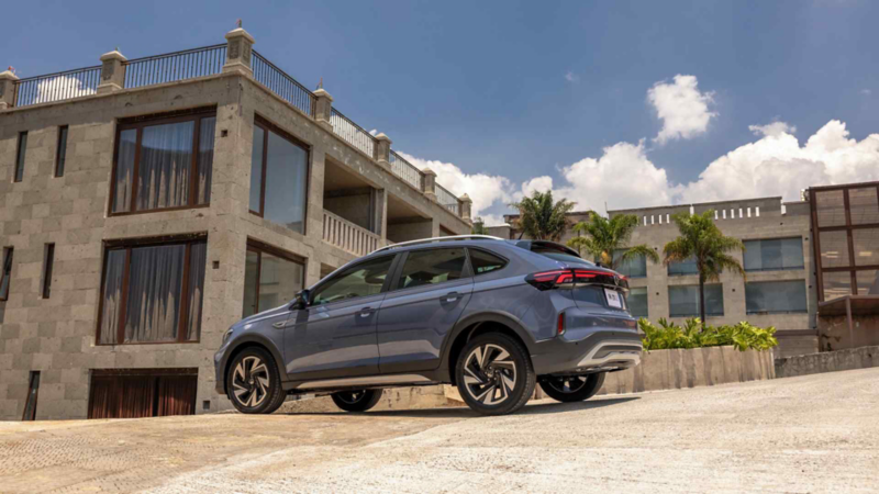 Volkswagen Nivus en color azul oscuro circula frente a conjunto de departamentos modernos. 