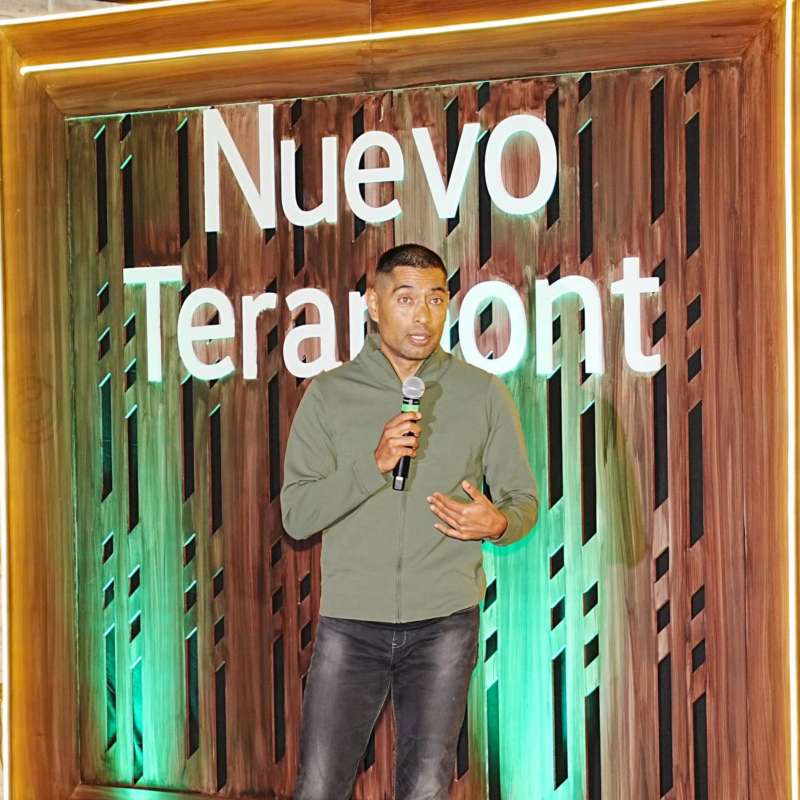Directivo de Volkswagen con micrófono presenta Nuevo Teramont ante un escenario de madera, luces verdes y letras del evento.