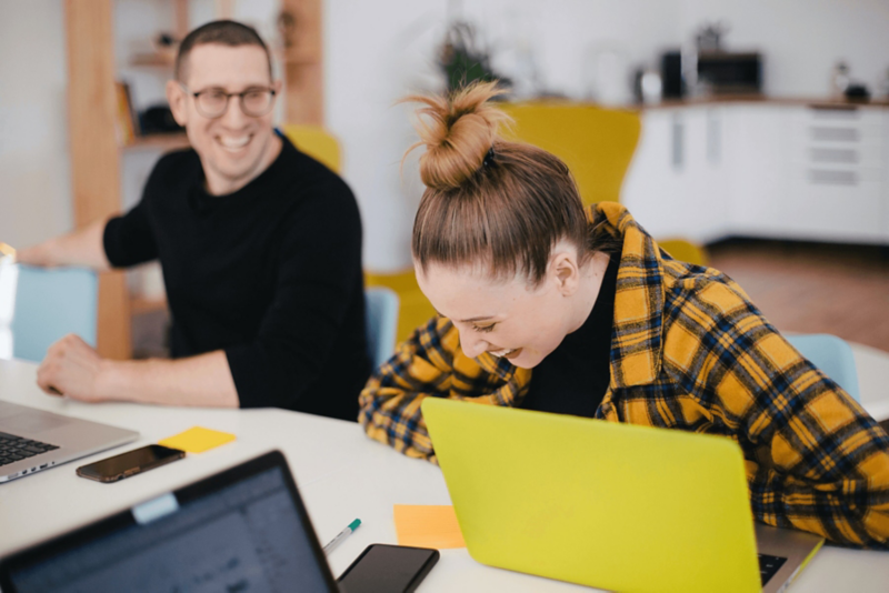 Zwei VW Mitarbeitende in der Cyber Security arbeiten lachend an Laptops in einem Büro