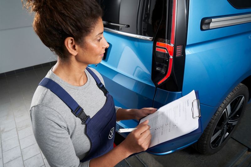 femme qui valide les points de controle garantie VW devant un Caddy bleu
