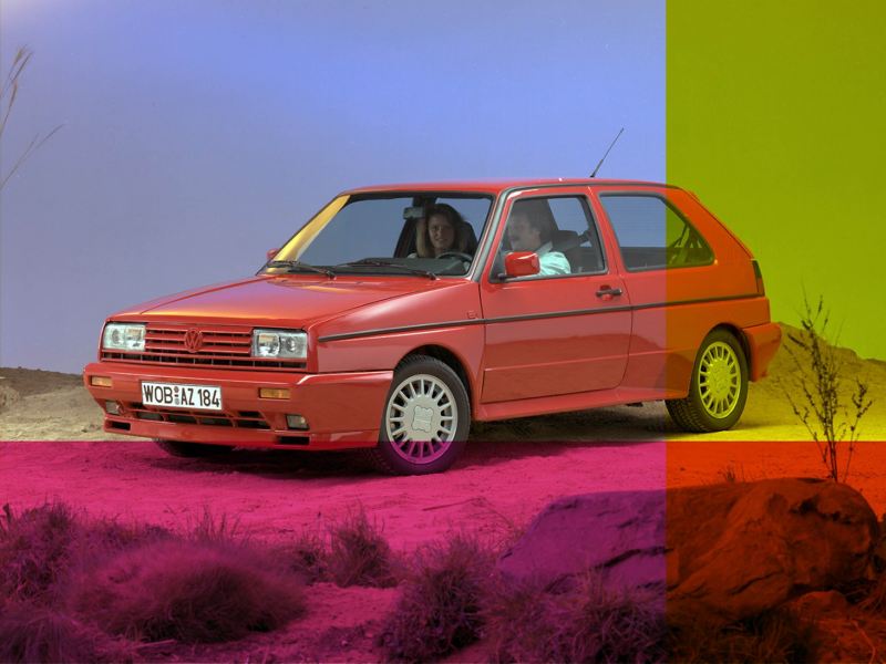 2 passengers sit inside a red Golf mark 2 on a desert like road