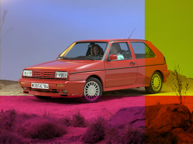 2 passengers sit inside a red Golf mark 2 on a desert like road