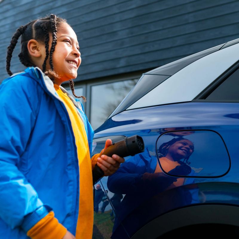 Child helping to charge blue Volkswagen family car