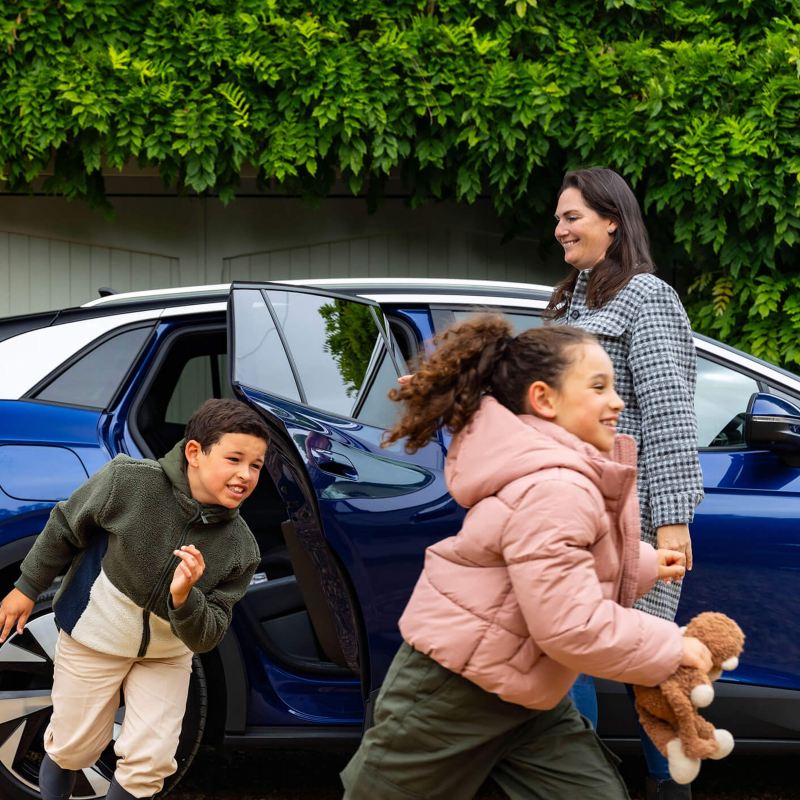 A mother holding open the door of an ID.4 and two children running around the car