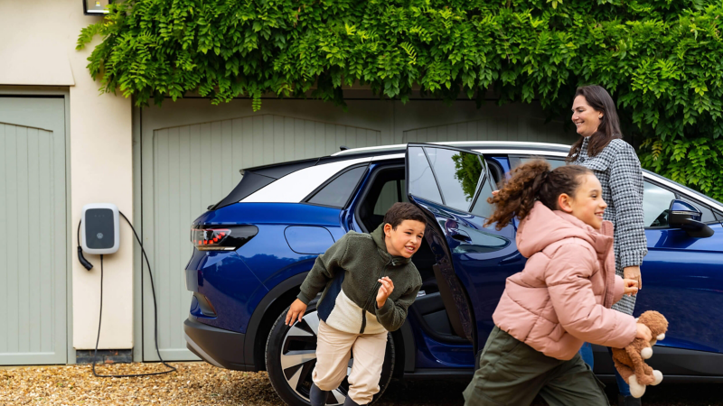 A mother holding open the door of an ID.4 and two children running around the car