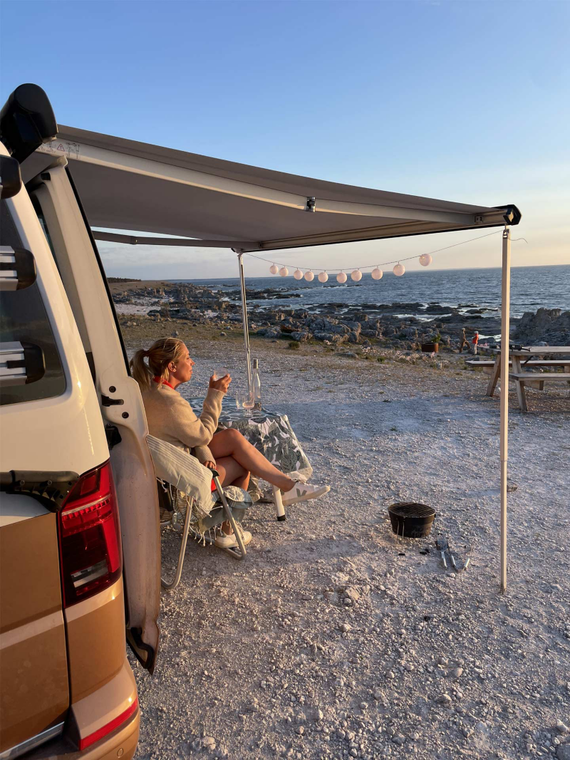 Lina Skandevall under markisen på sin VW California Ocean på en stenig strand.