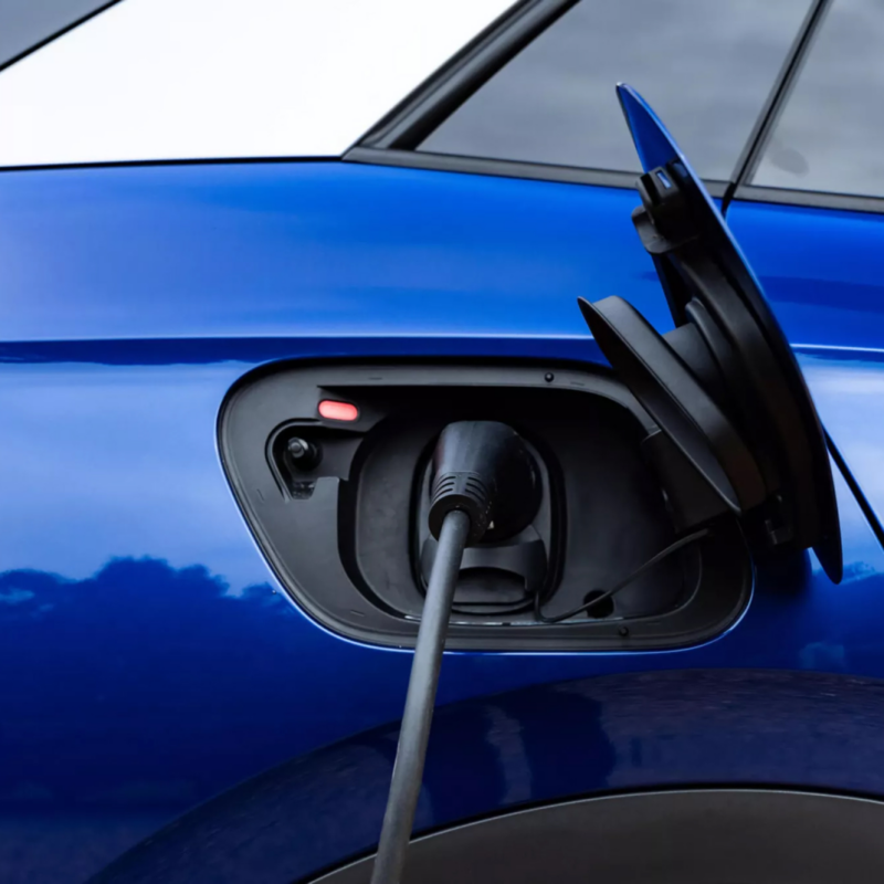 A close-up shot of a blue electric vehicle with its charging port door open, plugged into a charging cable.