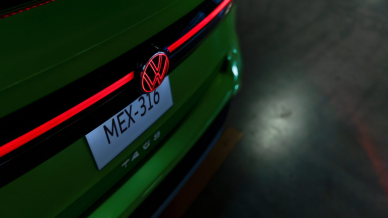 VW Taos verde por la parte trasera durante la noche, con emblema y barra de luz roja en primer plano.