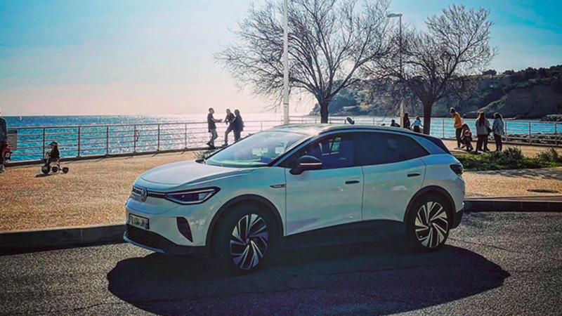 Volkswagen ID.4 blanche stationnée devant la mer un jour ensoleillé. 