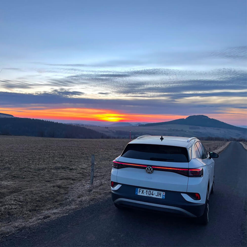 ID.4 blanche sur une route avec la bande LED arrière allumée et un couché de soleil en arrière plan.