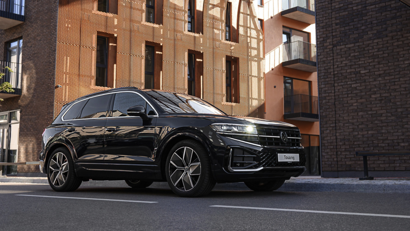 A VW Touareg R-Line parked at the roadside, diagonal view from above of the rear and panoramic sunroof.