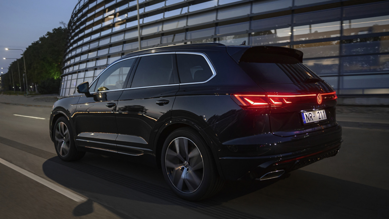 A VW Touareg R-Line parked at the roadside, diagonal view from above of the rear and panoramic sunroof.