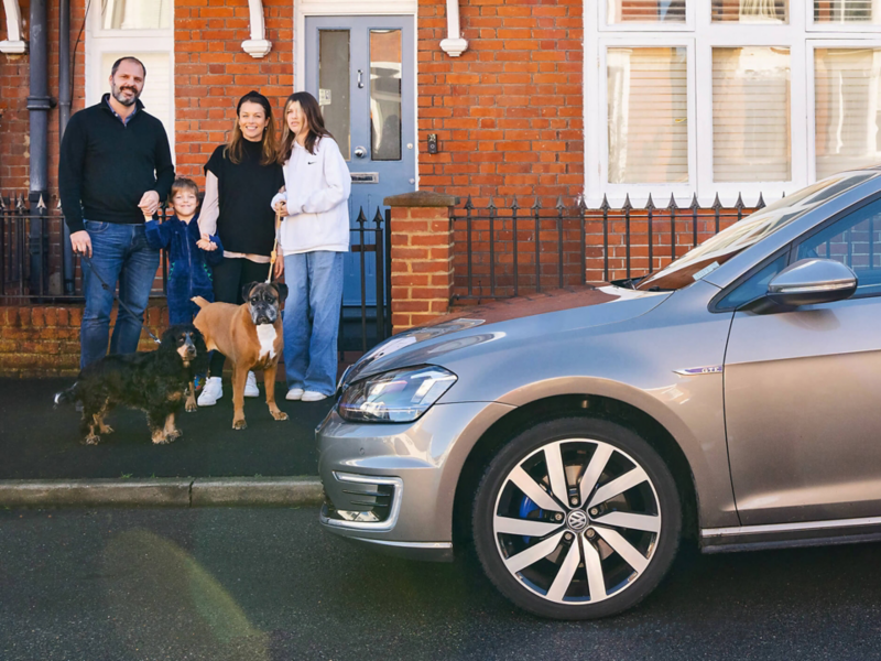 A family and their 2 dogs stand on the pavement outside their house next to a Golf GTE