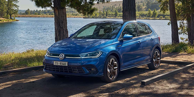 Blaue Volkswagen Polo am Ufer eines Sees in natürlicher Umgebung.