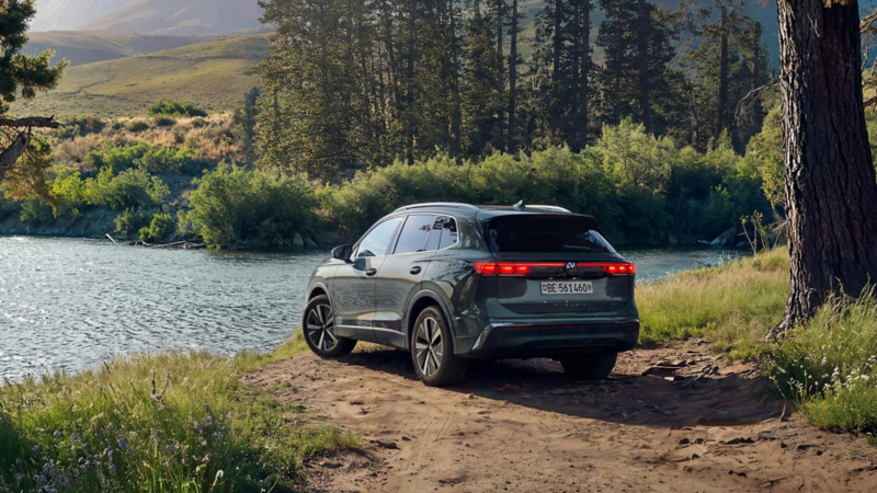 Dunkelgrüner Volkswagen Tiguan am Ufer eines Flusses in einer natürlichen Landschaft, von hinten schräg fotografiert.