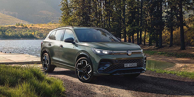Dunkelgrüner Volkswagen Tiguan PHEV in einer natürlichen Landschaft am Fluss.