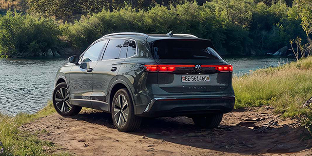 Dunkelgrüner Volkswagen Tiguan am Ufer eines Flusses in einer natürlichen Landschaft, von hinten schräg fotografiert.
