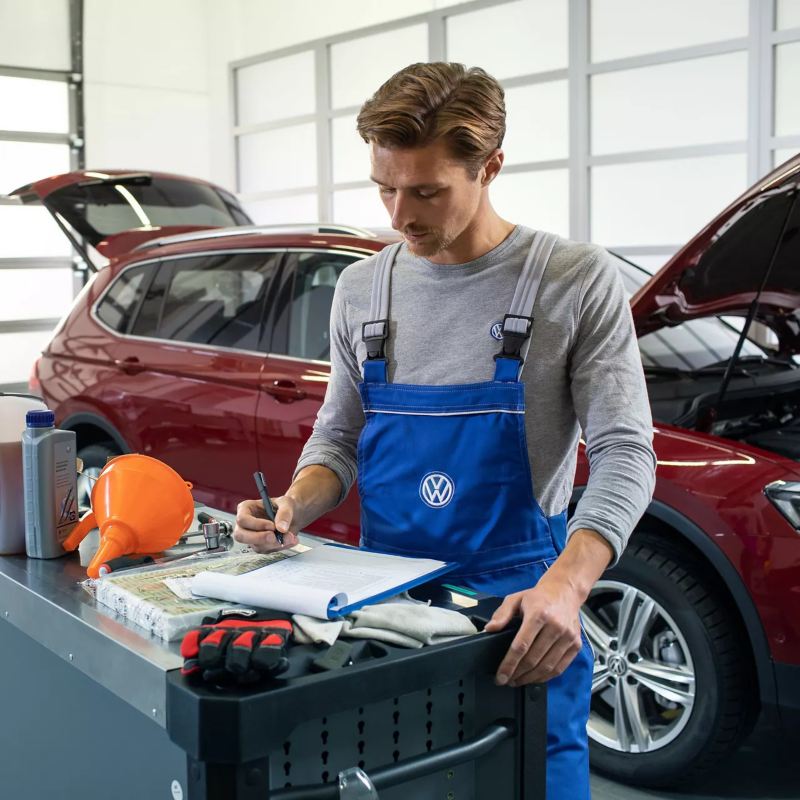 Homme en uniforme VW regardant le rapport, lien vers la page « Service » de VW