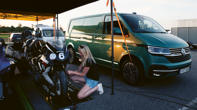 Roadracingstjärnan Malin Kullberg mekar med biken bredvid en VW Transporter Skåp