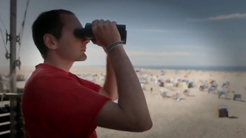 En livredder på en strand der kigger i kikkert