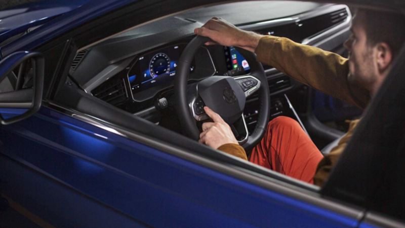 Hombre maneja un auto Volkswagen sedán color azul, con cuadro digital de instrumentos. 