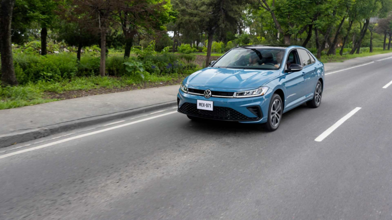 Volkswagen Jetta versión Sportline en color exterior azul circula sobre avenida con jardinera. 
