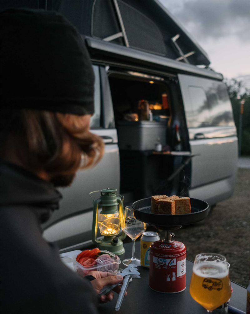 Sebastian vid det uppfällda campingbordet fullt med mat utanför VW California husbil.