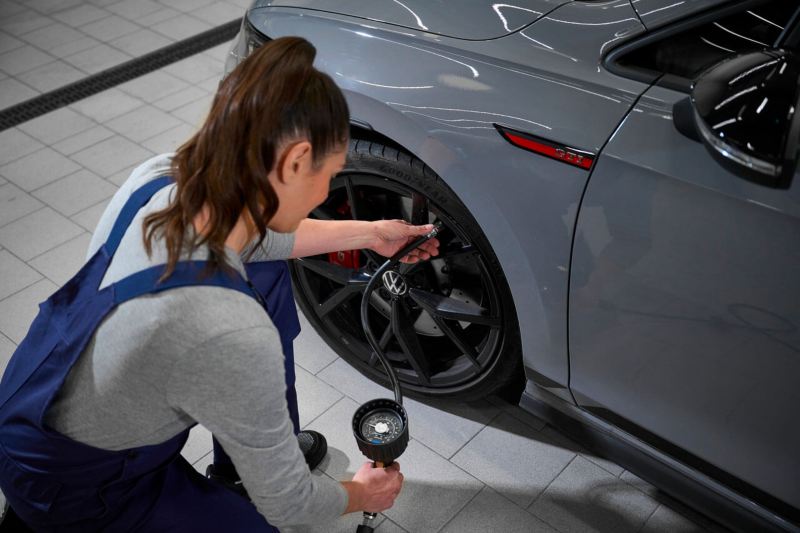 Un technicien Volkswagen et une femme discutent au milieu des véhicules présents dans l'atelier.