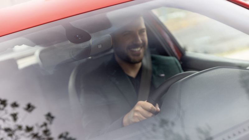 Conductor de un auto Volkswagen con cinturón de seguridad puesto sonríe mientras maneja.