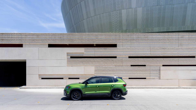 VW Taos verde estacionado de perfil frente a la fachada de piedra de un edificio moderno.
